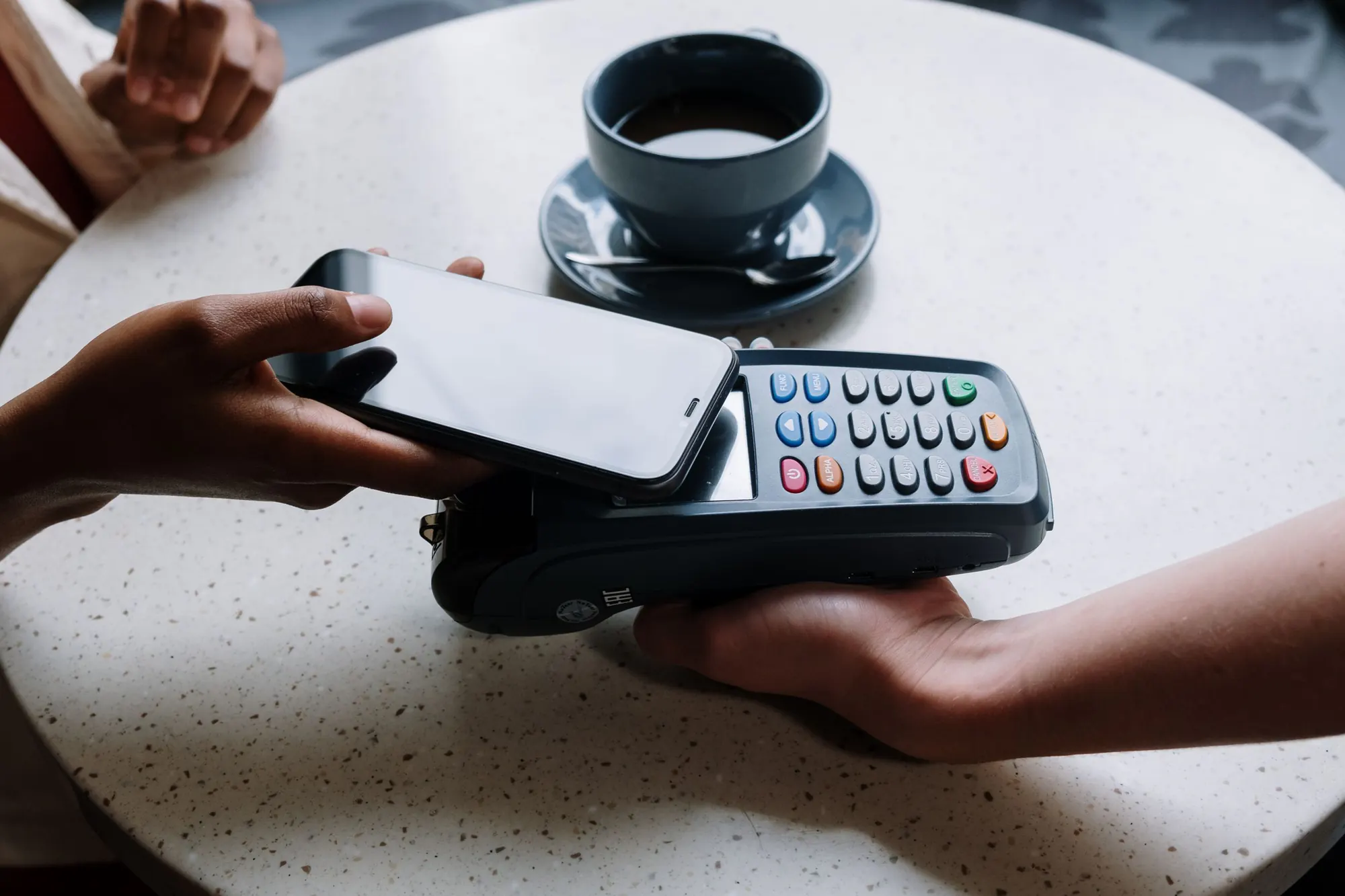 En gæst holder sin telefon mod en kortterminal og betaler ved et lyst cafébord med en kop kaffe