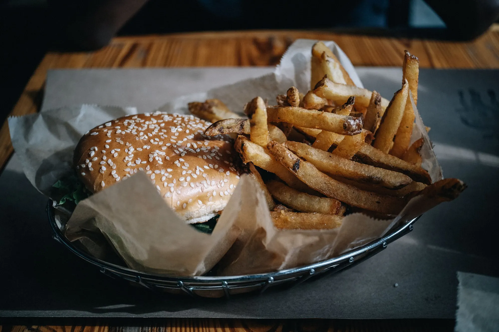 En burger med sesambolle og en stor portion pommes frites i en trådkurv med bagepapir