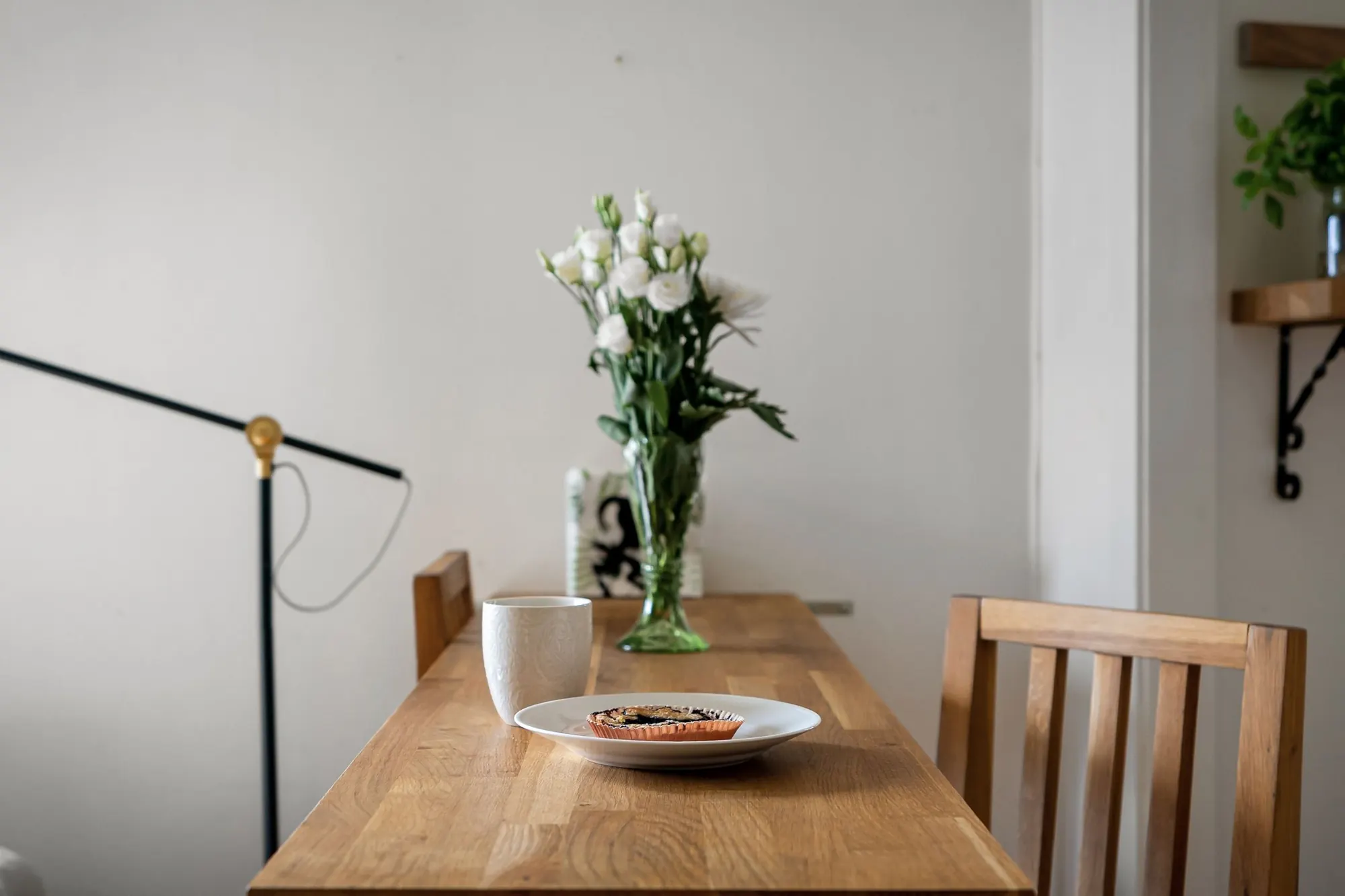 Et enkelt træbord med en kop, en lille tærte og en vase med hvide blomster i et lyst, nordisk rum