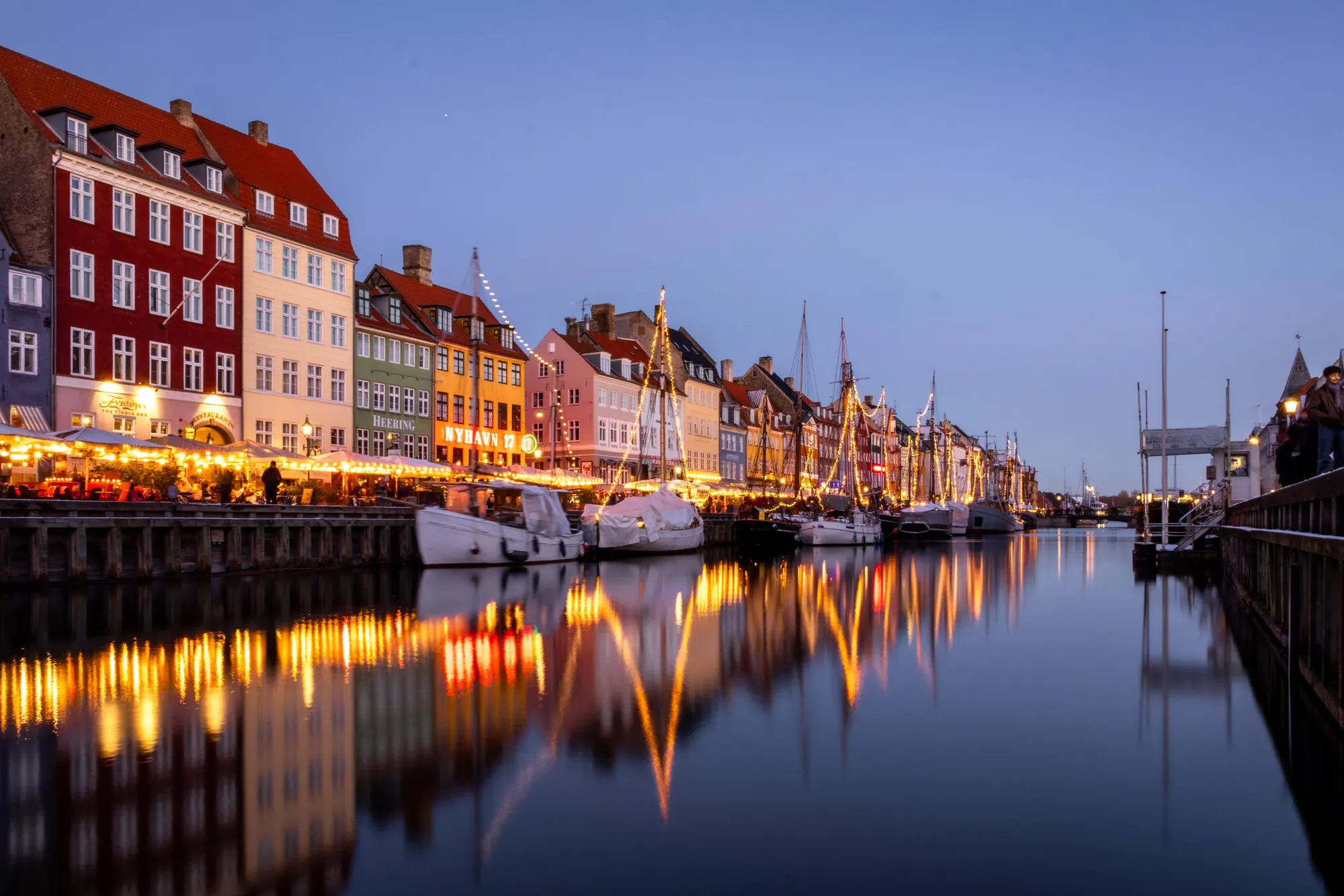Nyhavn i København i den blå time med oplyste restauranter, træskibe og lysene spejlet i kanalen