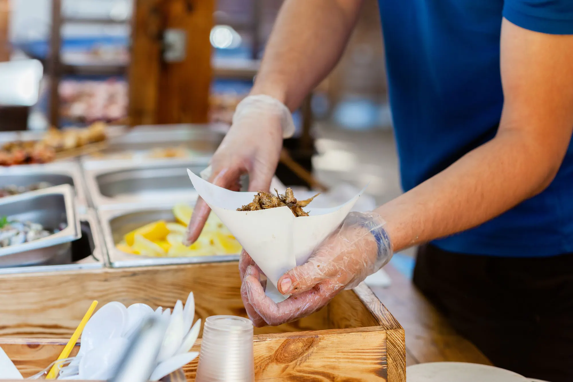 En kok med plastikhandsker fylder friturestegt fisk i et kræmmerhus af papir ved en street food-bod